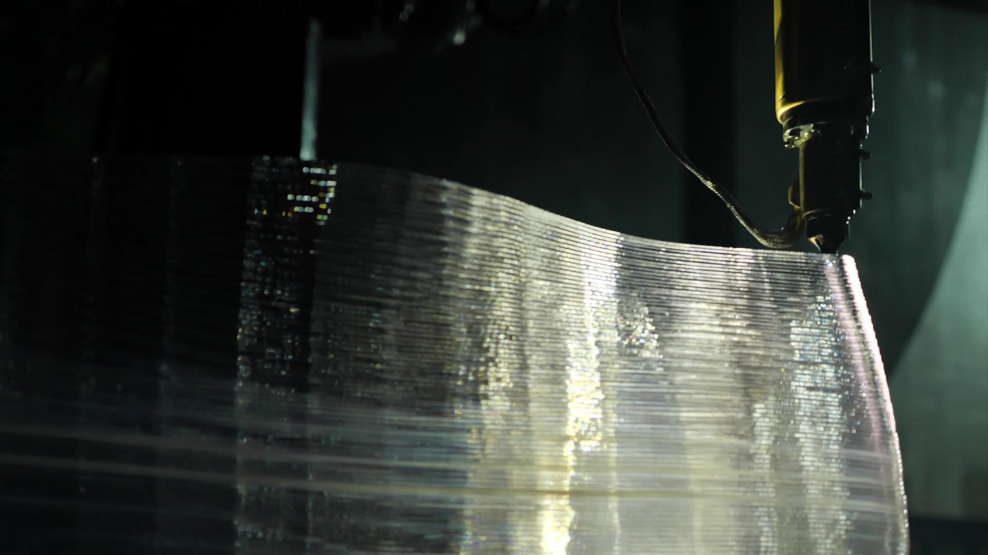 Close view of the robotic tool head and the layered translucent print surface.